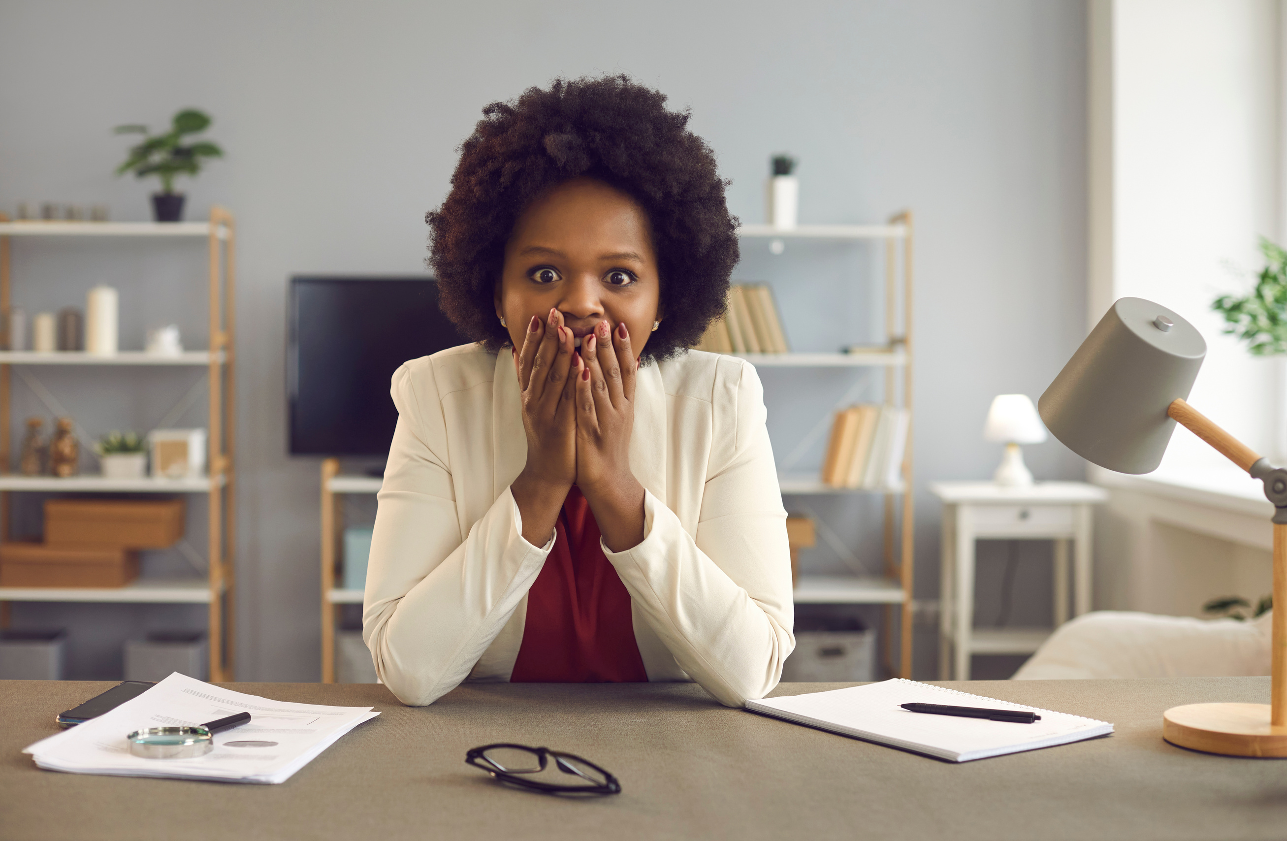 Portrait of Shocked African American Woman Covering Mouth with Hands Sit at Desk